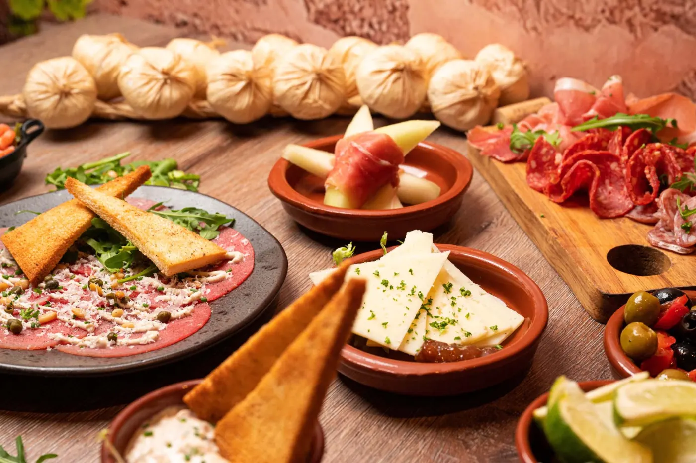 Carpaccio met toast, manchego, meloen met ham en een plank vleeswaren op een houten tafel