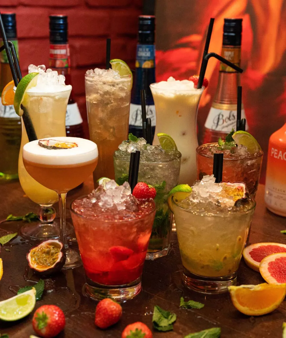 Een rij cocktails en mocktails met ijs, aardbeien en passievrucht op de bar