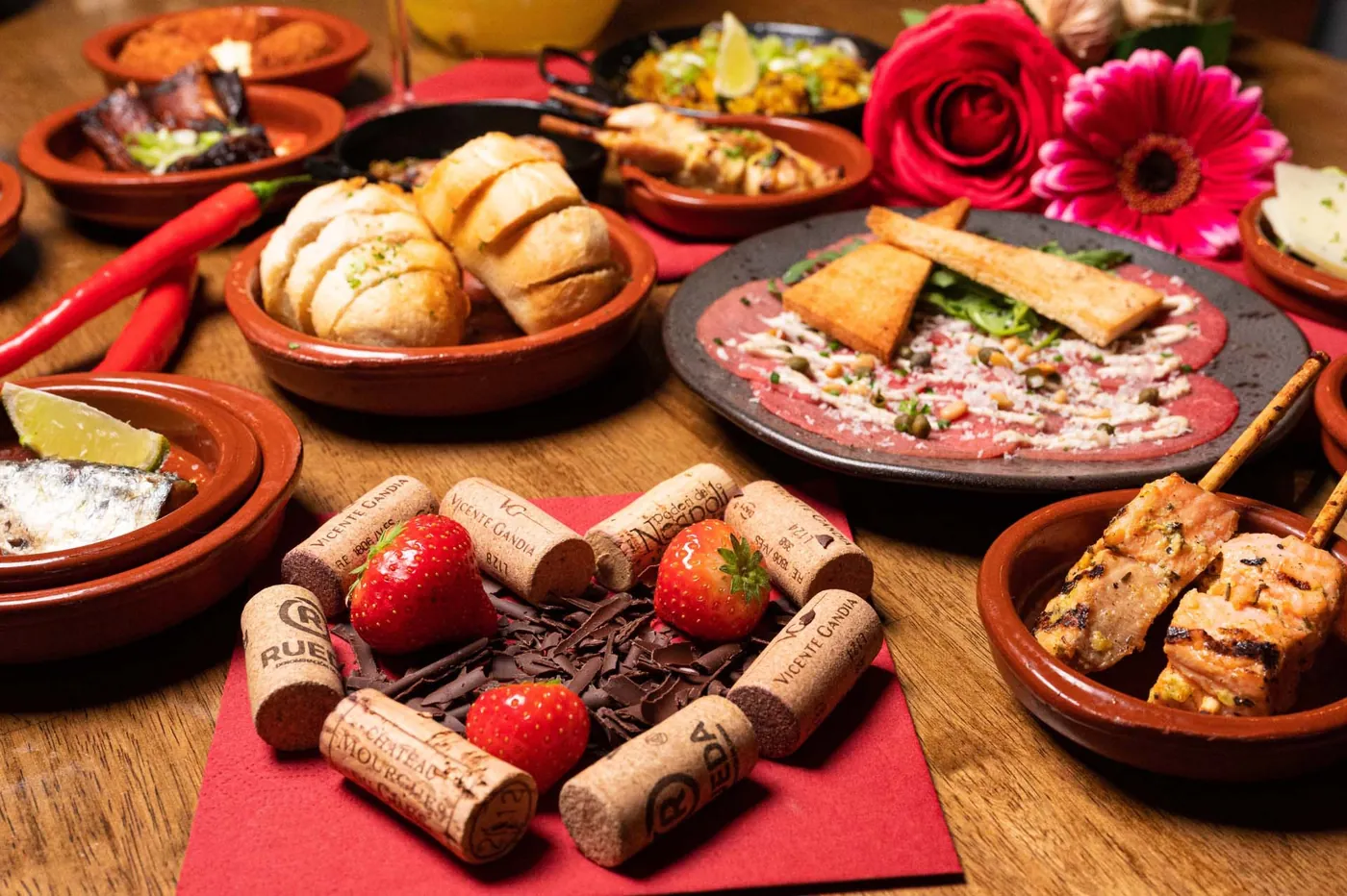 Terracotta schaaltjes met brood, carpaccio, spiesjes en aardbeien op een houten tafel